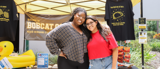 Two female students posing for a picture on PHSC's campus in front of welcome table